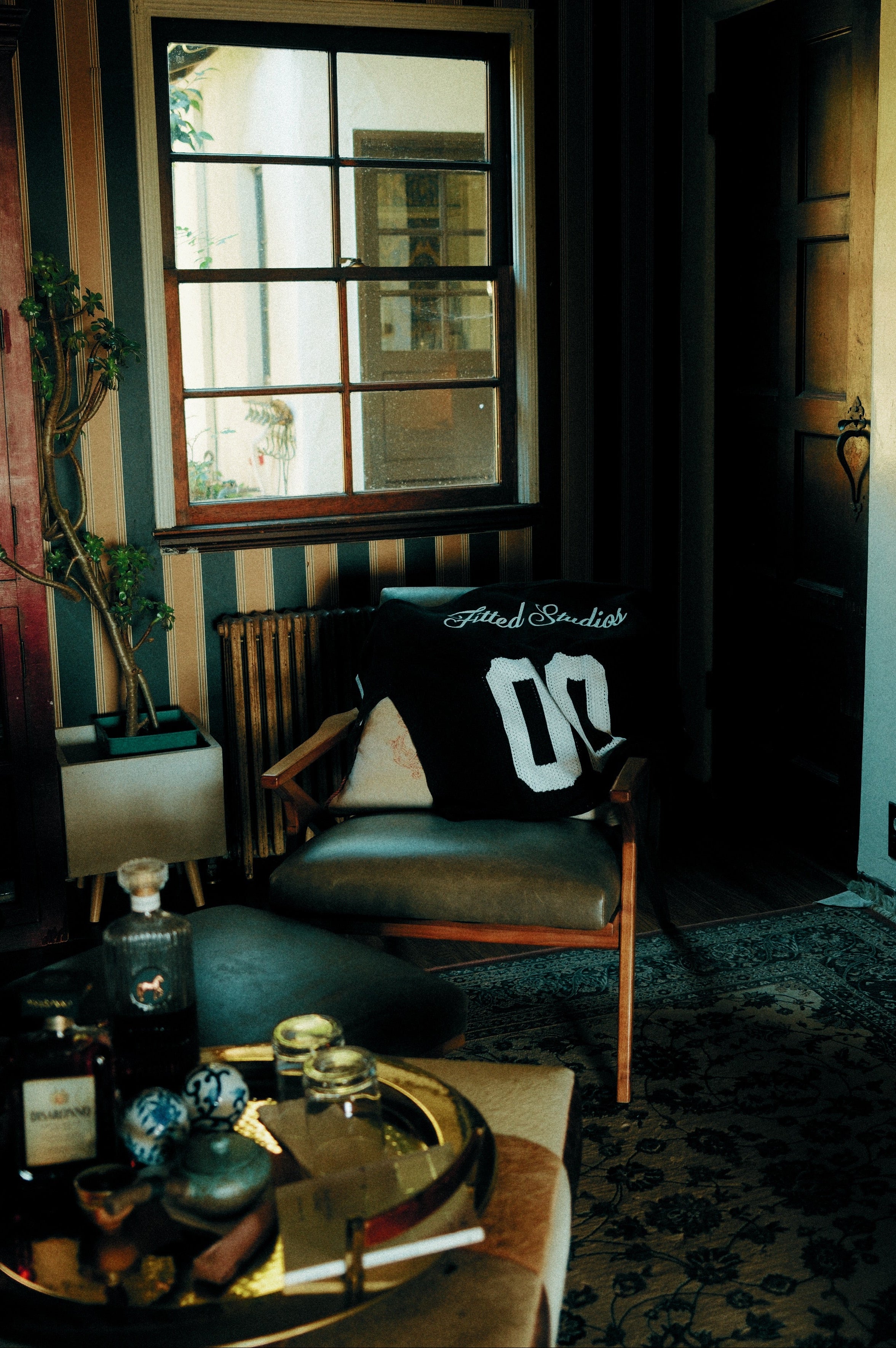 Dark room with a chair, table, and window with striped wallpaper.